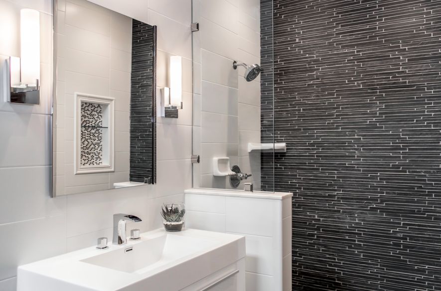Bathroom with white rectangular tiles ran horizontal and a natural state corinth in black on walls as accent. Marble transition used on top of knee wall.