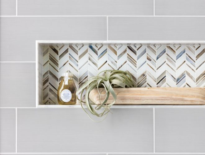 Recessed shelf with blue, brown, and white chevron mosaic. A plant and body wash sit on the shelf.