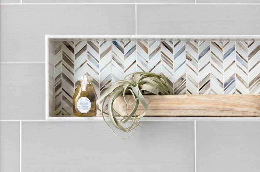 Recessed shelf with blue, brown, and white chevron mosaic. A plant and body wash sit on the shelf.