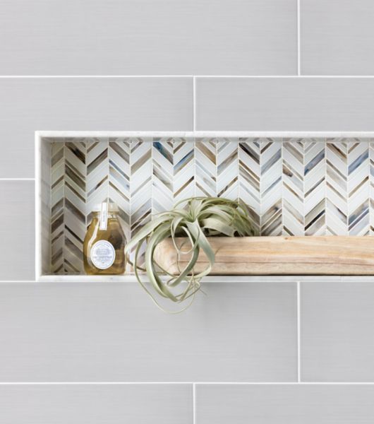 Recessed shelf with blue, brown, and white chevron mosaic. A plant and body wash sit on the shelf.