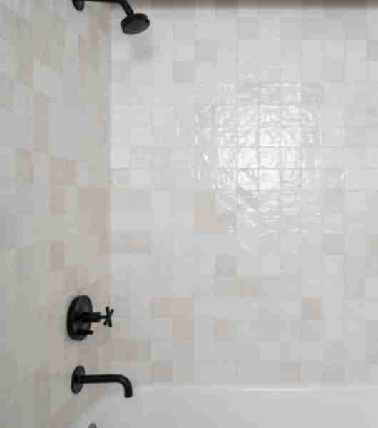 Combined shower and bath featuring a white tub, white handmade-look ceramic tile on the shower walls, and matte black shower fixtures.