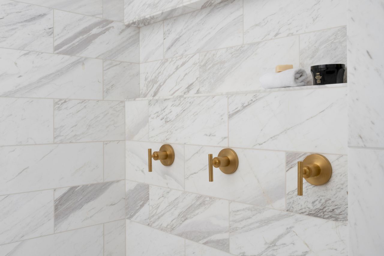 Shower with brass fixtures and rectangular white marble with soft grey veining tile wall.