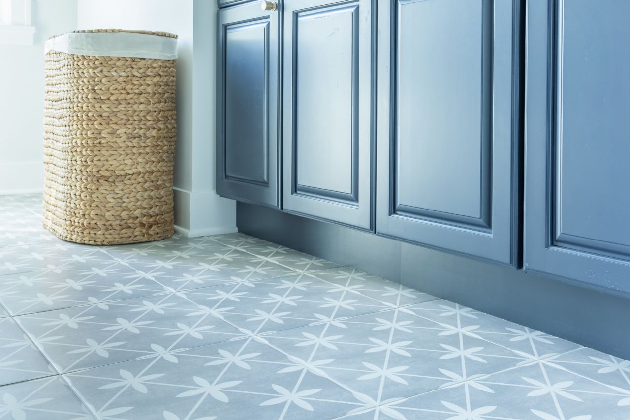 A laundry room features blue cabinets and floor covered in square ceramic tiles with a blue and white motif.