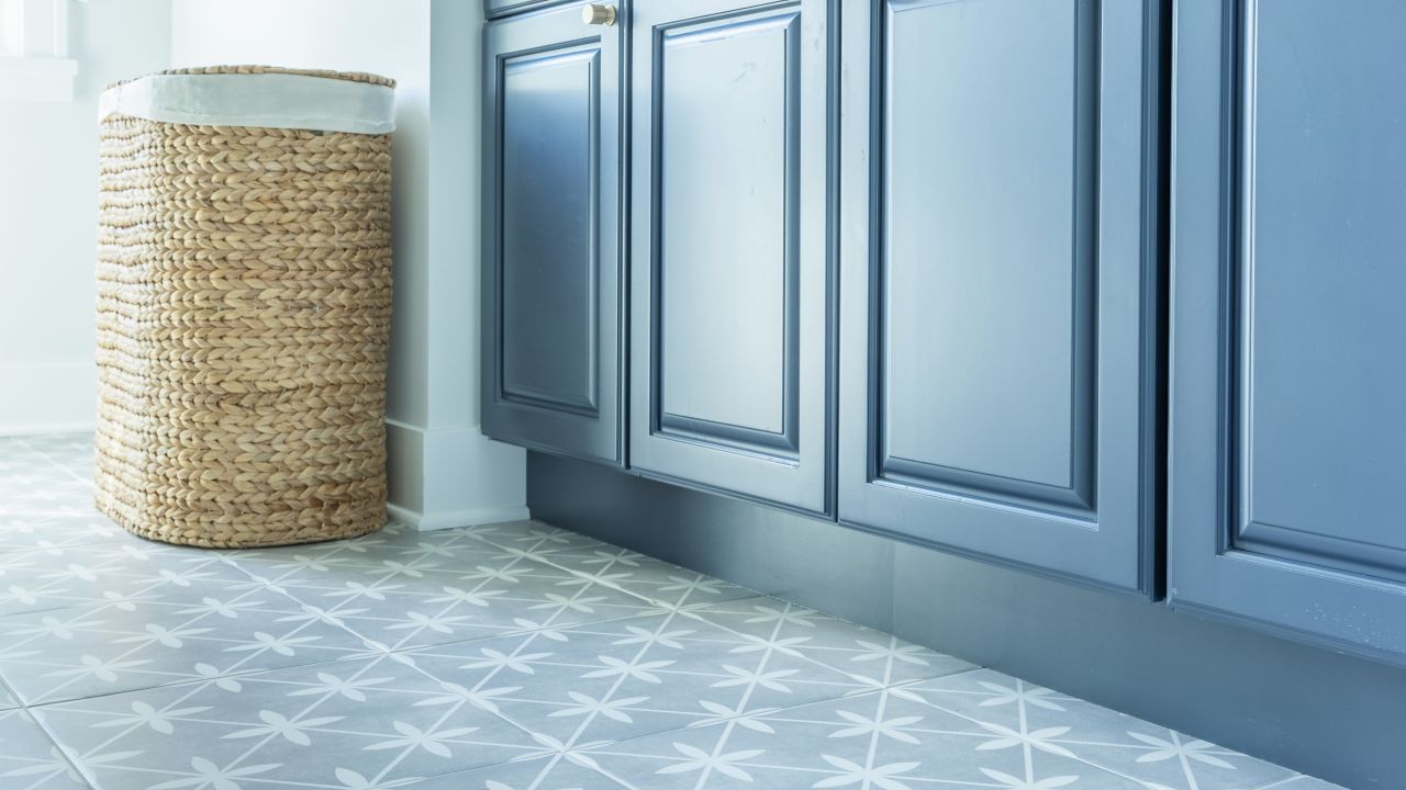 A laundry room features blue cabinets and floor covered in square ceramic tiles with a blue and white motif.