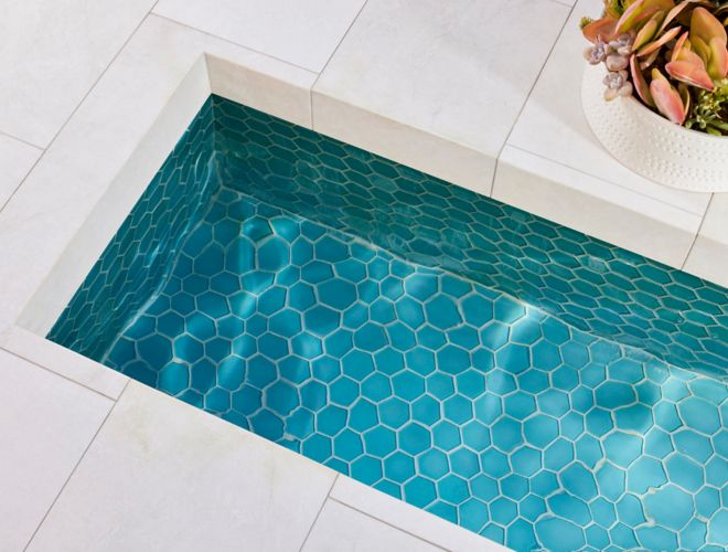 Blue glass tile in the bottom of a fountain surrounded by white tiles and a potted plant..