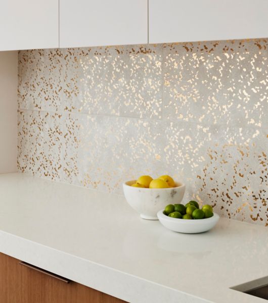 White counter top with bowls of fruit and a white and gold tiled wall