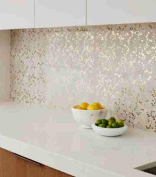 White counter top with bowls of fruit and a white and gold tiled wall