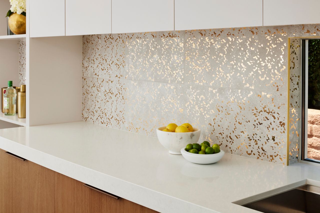 White counter top with bowls of fruit and a white and gold tiled wall