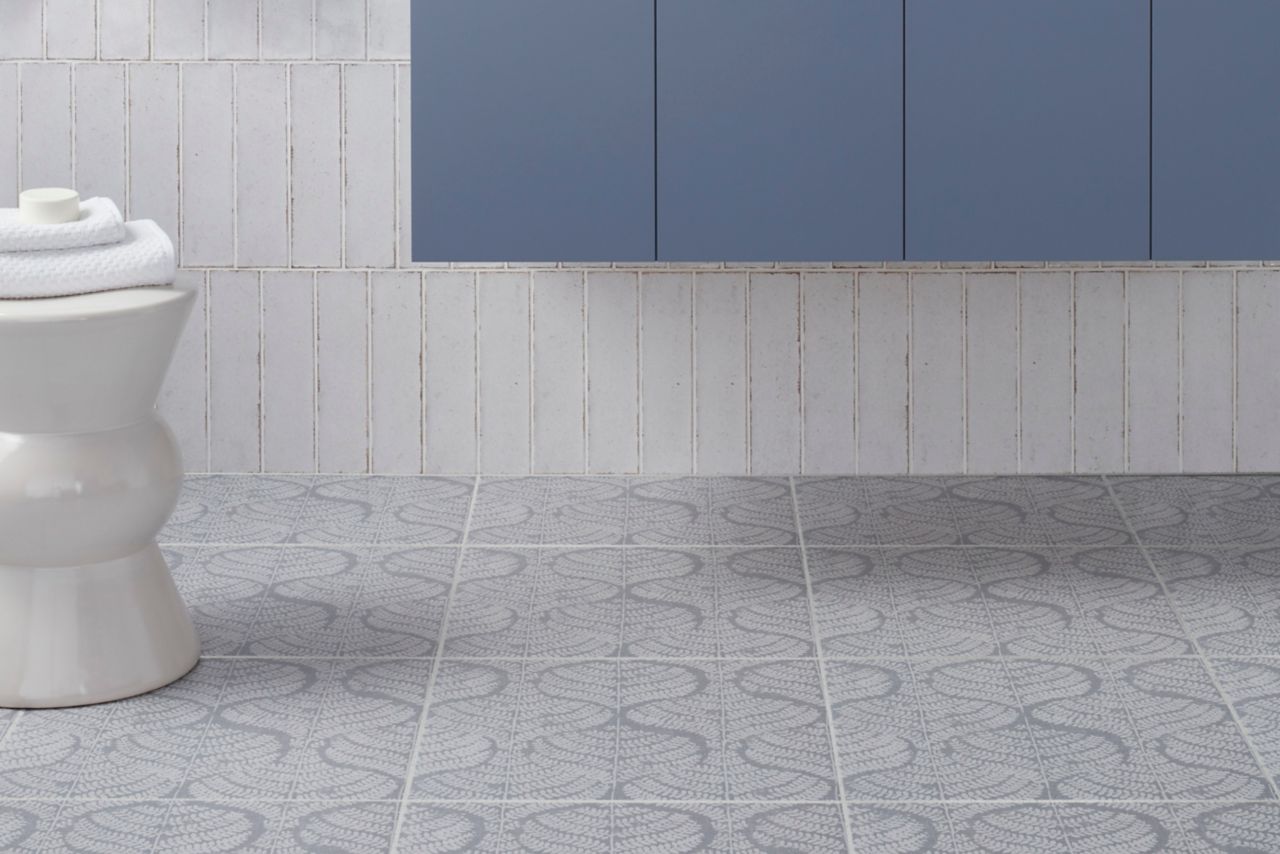 This bright and cheery bathroom features a white handmade-look subway tile walls and white and blue fern patterned floor tile. 