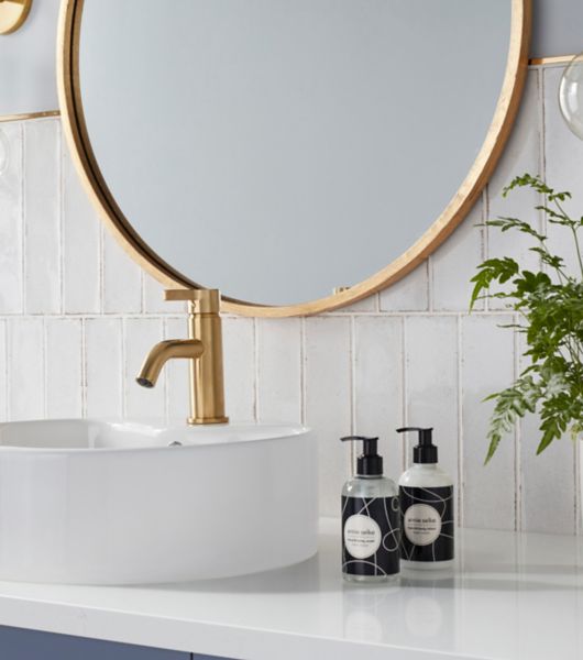 Bathroom sink backsplash featuring white subway tiles that run vertically on the wall above the white counter and sink.