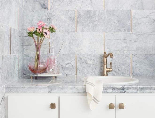 Sophisticated white and grey carrara marble wall with gold accents on kitchen backsplash.