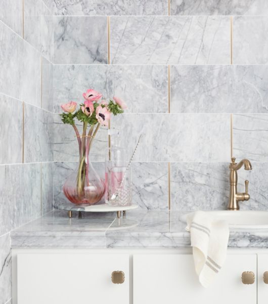 Sophisticated white and grey carrara marble wall with gold accents on kitchen backsplash.