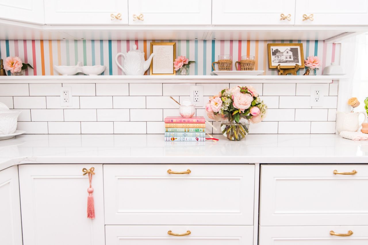 Kitchen with white subway tile backsplash, colorful striped wallpaper and white cabinets.