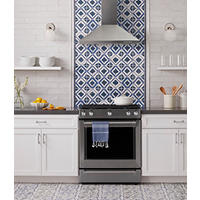 Thumbnail image of Kitchen area with with backsplash and floor tiled back slash is child in a long subway tile with a natural edge accent behind stove uses tile transitions and blue and white to match decorative tile behind stove and hood flooring is done in a corresponding blue and white tile with different pattern countertop is a slate grey floating shelves and special lighting complete the look.
