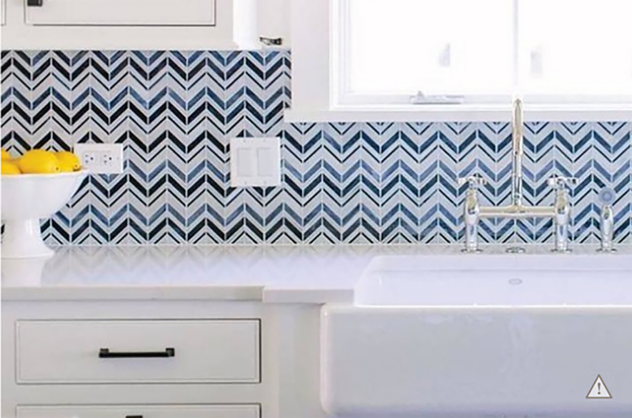 Blue zig-zag patterned tile backsplash with sink, white counters and bowl of lemons