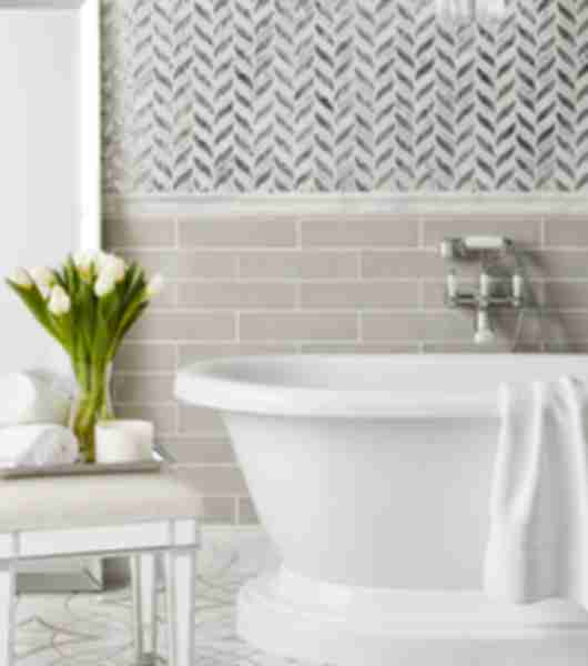 Bathroom with white tub, bench and flowers. Mosaic tile wall and patterned tile floor.