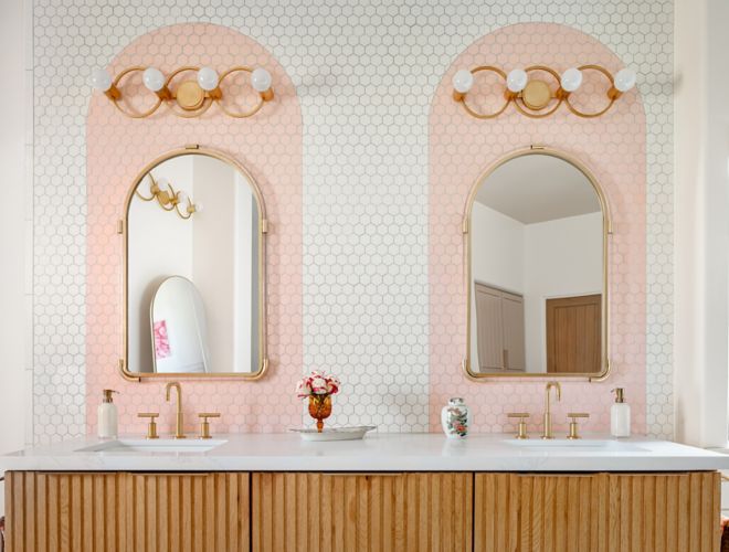 Double sink vanity with mirrors, gold light fixtures and white with pink arch tile