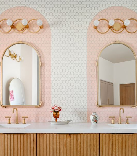 Double sink vanity with mirrors, gold light fixtures and white with pink arch tile