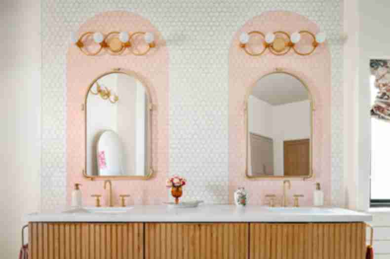 Double sink vanity with mirrors, gold light fixtures and white with pink arch tile
