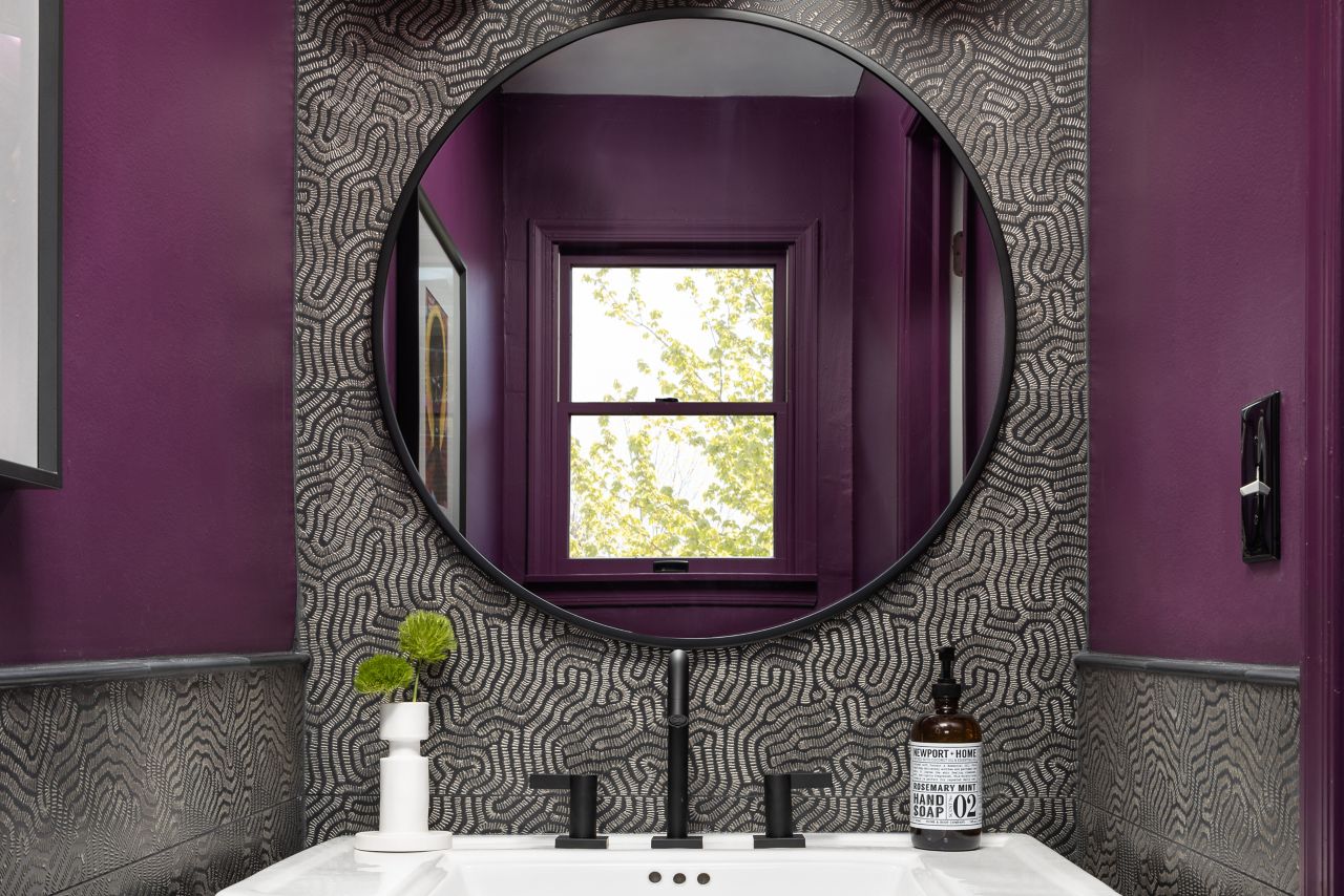 Dark purple and black and gold tile sink backsplash. White sink and circular mirror.