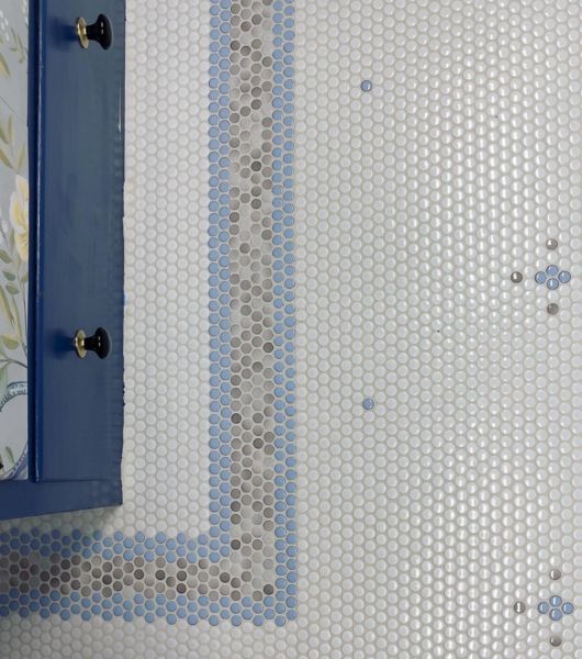 Overhead view of floor with white, blue and grey penny round tiles in a pattern with a border and repeated flower shapes.
