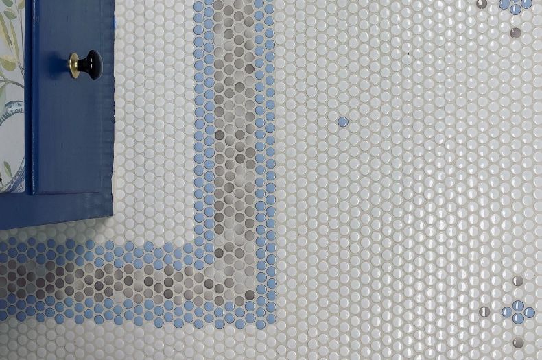 Overhead view of floor with white, blue and grey penny round tiles in a pattern with a border and repeated flower shapes.