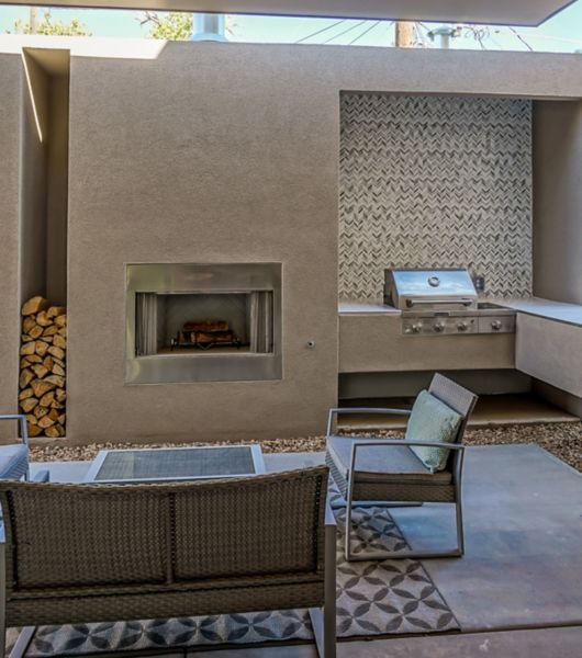 Outdoor area with chairs and sofa with a light-brown tiled wall featuring a fireplace and grill with mosaic tile accent wall.