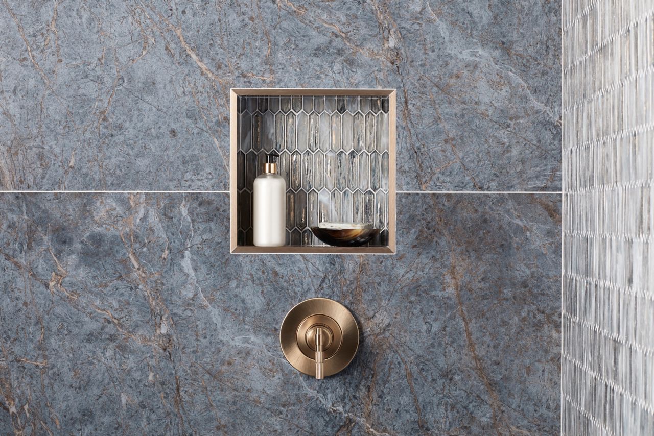 Detail view of shower walls and recessed shelf with porcelain marble patterned large format wall tile in blue/grey and neutral tans.  Glass mosaic used to accent niche and accent wall.  