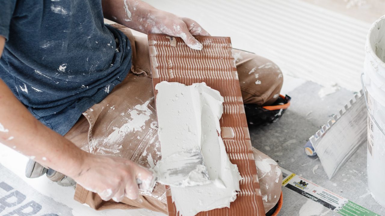Worker spreading thinset mortar onto the back of a tile before installation on a floor.