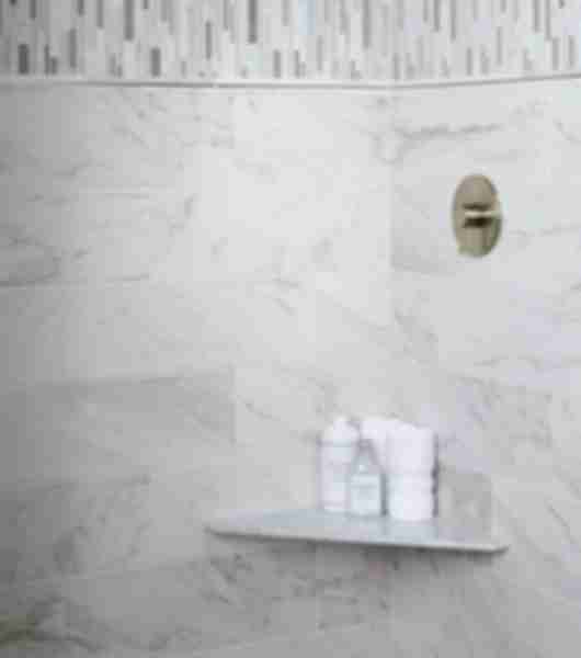 Walk in shower with natural stone accents and trim with marble looking ceramic wall tile, mosaic accent vertically ran on upper wall divided by marble and stainless trim pieces. A Marble corner seat adds function and elegance to the shower.