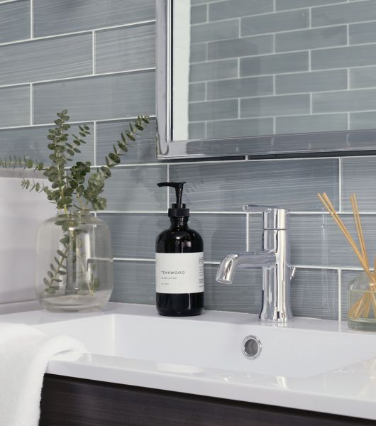 Vanity area with knee wall all tiled in cool tones in variations of black white and greys. Some soft tans and blue hues accent and add balance to the pallet.  White tile on knee wall capped in marble terminate into glass subway tile backsplash. Sink is gloss white. Fixtures are polished chrome.