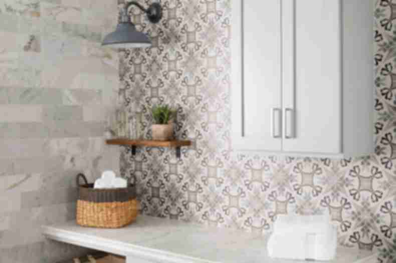 Tiled walls in  white marble tile and a patterned porcelain tile.  Each wall is tiled differently and accents the white marble counter and light cabinets.