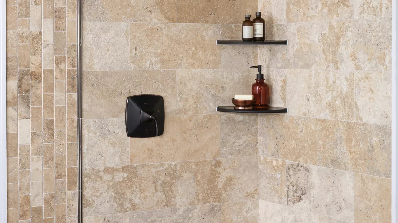 Walk In shower tiled in natural travertine stone with metallic profiles and corner shelves.