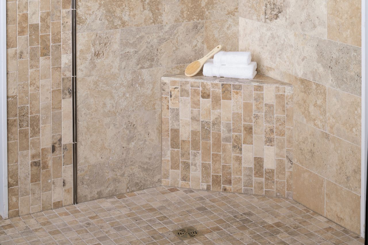 Walk In shower tiled in natural travertine stone with metallic profiles and corner shelves.