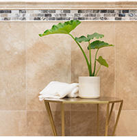 Thumbnail image of Travertine tile and profiles in polished finish and beige natural tones with onyx border accent make up wainscotting behind small table and potted plant.