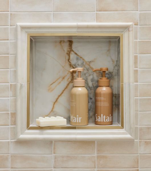 This chic shower niche features glossy and matte beige subway tile and a gold and grey veined marble-look tile and marble and gold trim. 