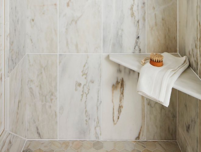 Beautiful polished marble shower with grey and gold veining, a shower niche and corner seat.