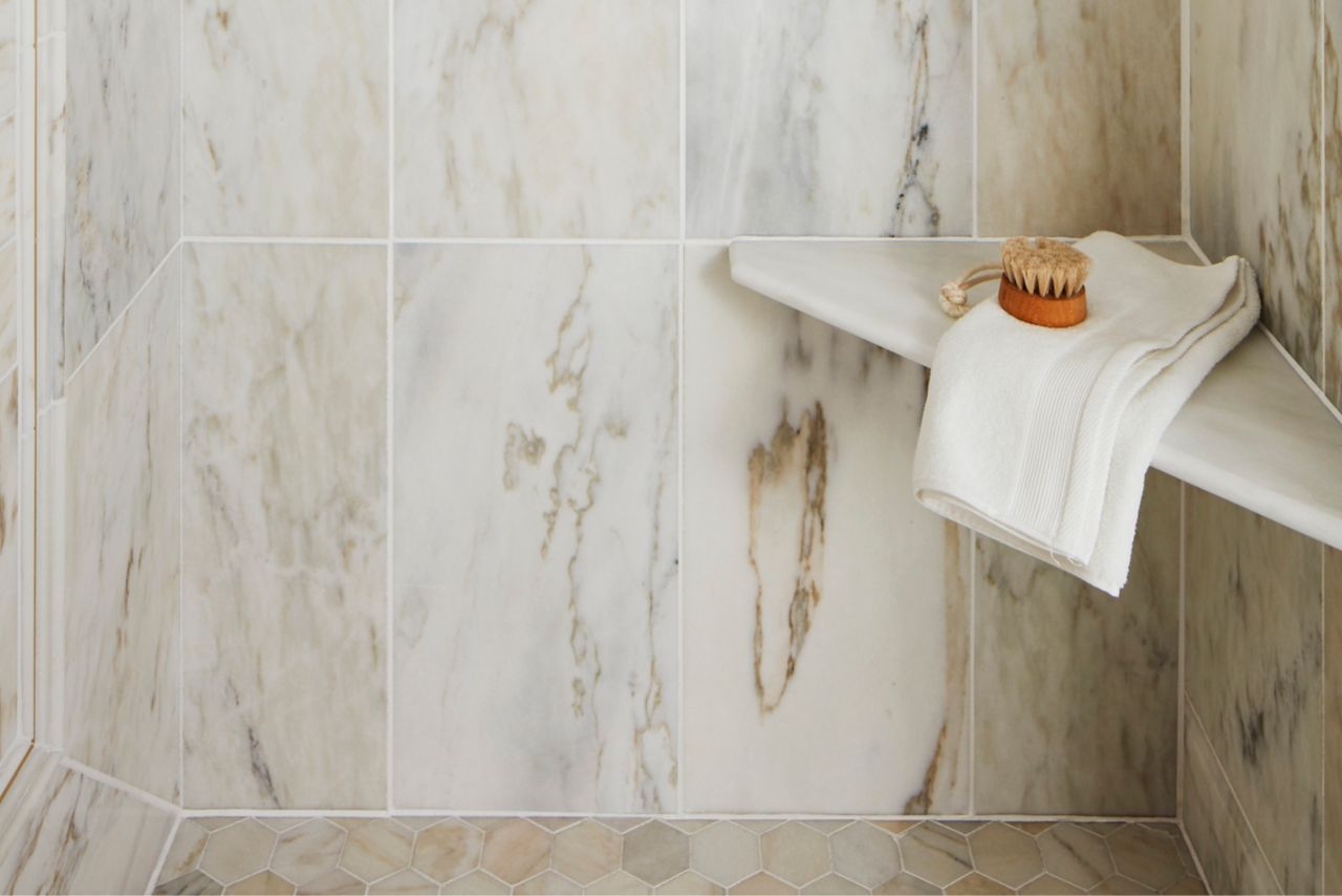 Beautiful polished marble shower with grey and gold veining, a shower niche and corner seat.