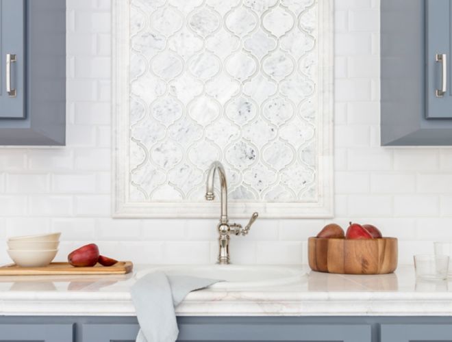 Kitchen with blue cabinets and white marble arabesque backsplash above sink.