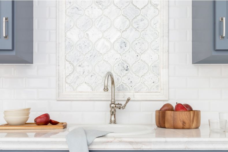 Kitchen with blue cabinets and white marble arabesque backsplash above sink.