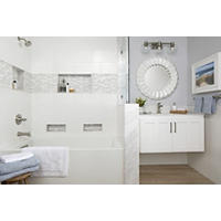 Thumbnail image of Featuring a tiled bathroom area with a faux wood tile in warm beiges on the floor Hampton Carrara marble in soft whites and light grey tones as finishings on knee wall with a glass partition on top recessed shelving done in a decorative mosaic glass with a crackled finish and white geometric shapes mosaic also used as a thick border accent and and tub surround wall tile is a ceramic in white large format rectangular staggered horizontally this area features brushed metal silver fixtures with an unique round mirror and decorative artwork above a floating white vanity.