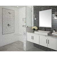Thumbnail image of Bathroom area utilizing several different tiles to make a unique look glass subway tile behind vanity offsets the lighter Carrera grass ceramic marble look and marble features used in this area a picture framed cobble tile is used to showcase the fixtures and there is decorative tile and recessed shelves is slender Carrera marble seat is set in tile to give both storage and accessibility shower itself is curbless with a trench drain the floor tile is large 12 by 24 tiles that also resemble marble this is a transitional space with beautiful greys whites and cream tones.