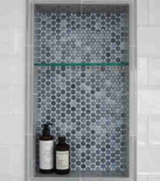 Featuring a detailed view of a shower niche 14 by 24 in size split in thirds with a glass shelf this niche is used for storing item in the shower area as seen here and is accented with grey penny round mosaic tile with a variety of shades.  Double gloss ceramic grey pencils border niche and white textured gloss subway tile is the wall tile here.