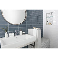 Thumbnail image of Bathroom area with walk-in shower vanity wall shares shower wall in a large 4 by 12 inch subway tile a framed ceramic in a gloss finish other shower wall is tiled in a large format Bianca wave ceramic tile with a textured gloss white finish,  recessed niche is tiled with matching mosaic like the bench facealso using the same bullnose edges.  Mosaic accent is in a Chevron pattern. A round mirror and large white sink with metal frame to match Polished Chrome fixtures complete the space.