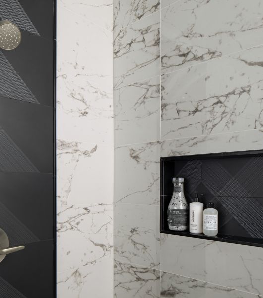 Modern shower with white marble tiled walls and black accent tiled shower niche.