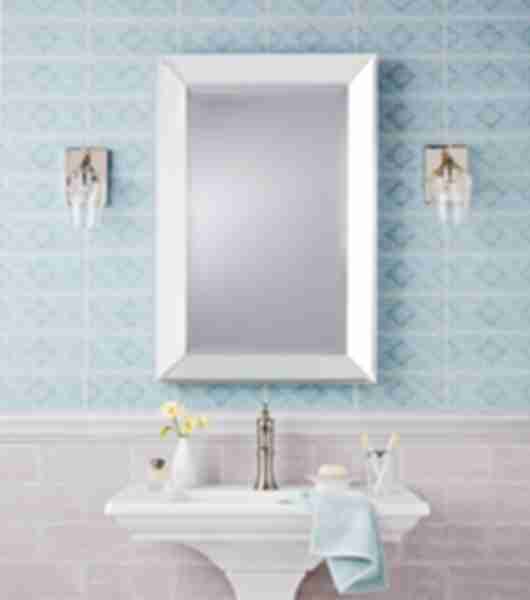 Bathroom area with wainscoting behind pedestal vanity two different tiles are used here although they are in the same family one features a pattern the other is a neutral subway tile in taupe with a coordinating chair rail to divide the lower and upper wall tile lower tile is staggered horizontally upper tile is stacked with blue patterned. A bbeveled edged mirror hangs above pedestal vanity and a warm metal is used on fixtures and coupled with glass features.
