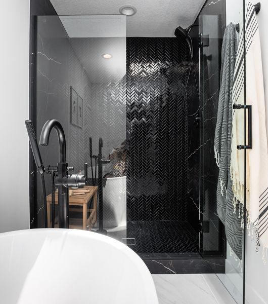 Herringbone mosaic tile in a glossy black creates movement and shine that draws the eye up from the floor to the walls of this shower.