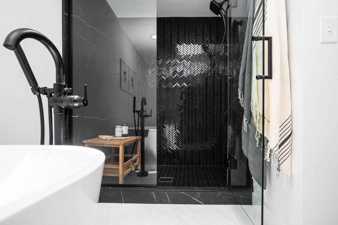 A shower with black herringbone patterned tile on the floor and walls.