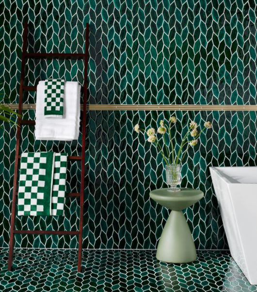 Green-leaf wall and floor tile with tub, towels and small green accent table with flowers.