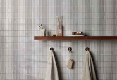 Bathroom wall tiled in long thin white tiles with a brown wood shelf holding toiletries